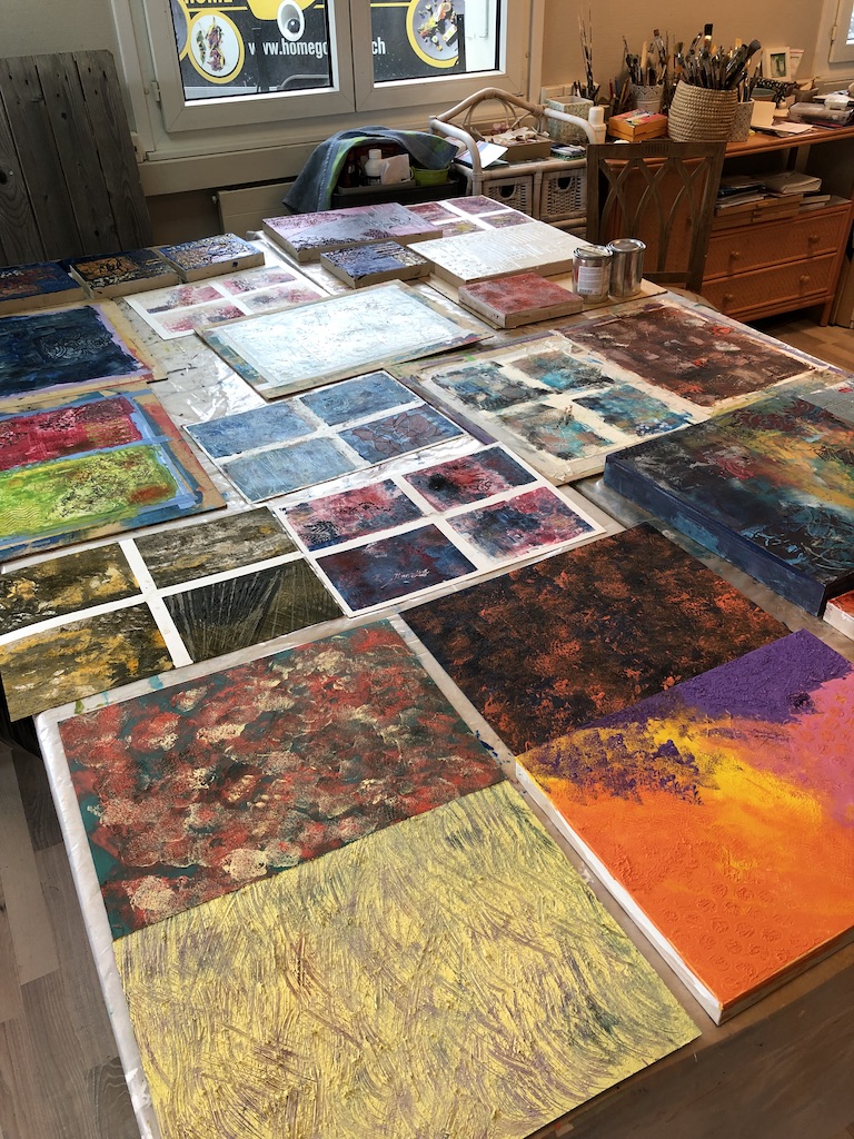 Colorful cold wax paintings spread across the table